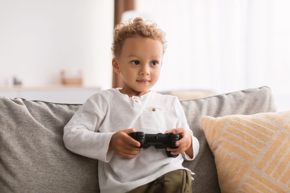 Young African Boy Having Fun Playing Videogame Sitting At Home